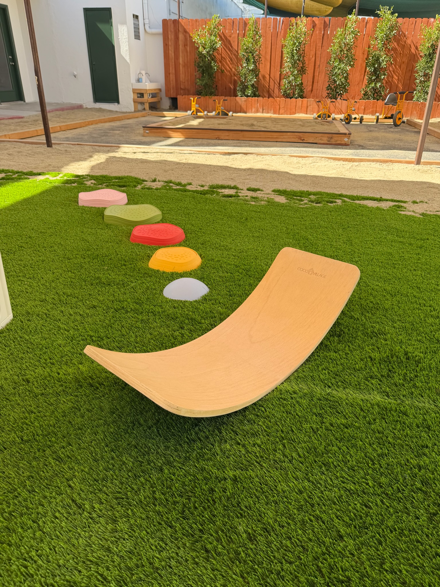 Happy Nook outdoor play yard — turf, balance board, stepping stones, and sandbox