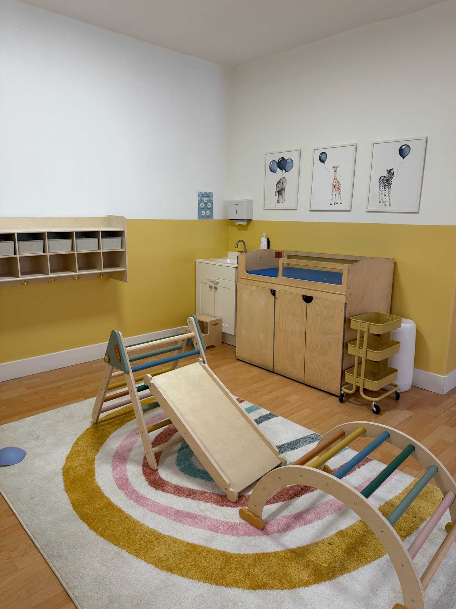 Inside Happy Nook — infant room with Pikler triangle and warm yellow walls