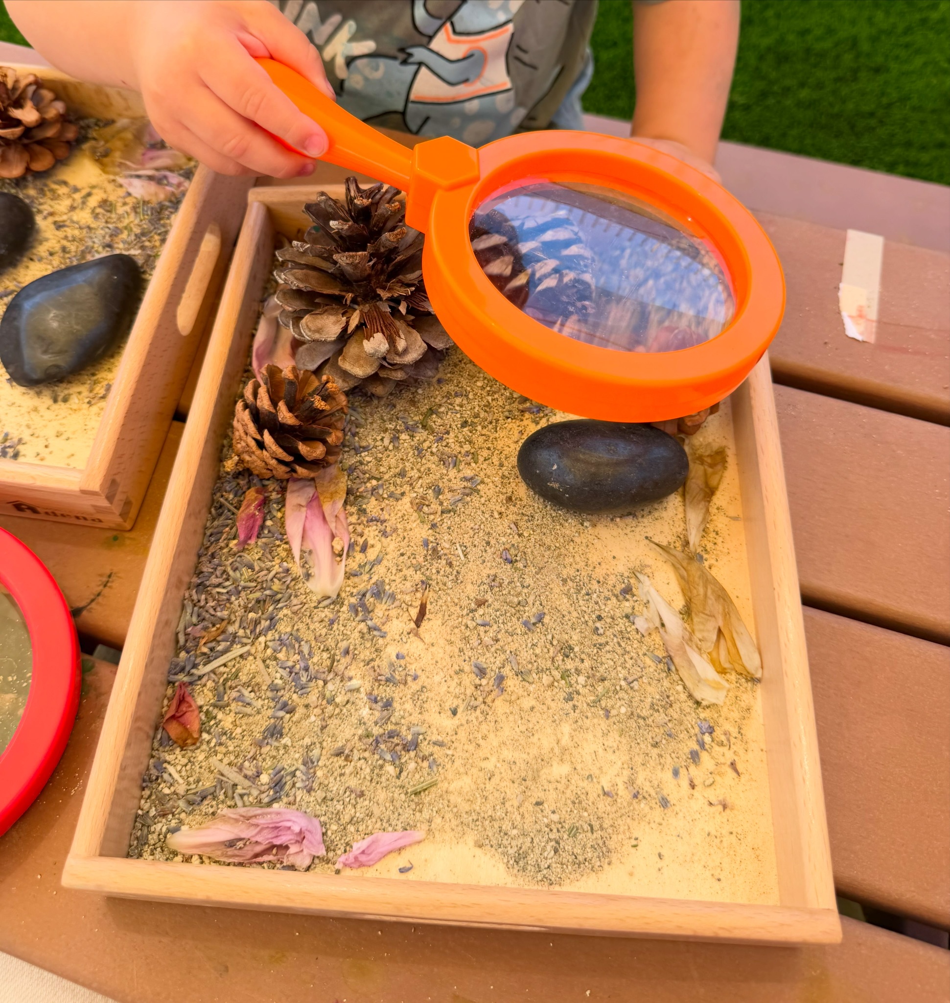 Child using a magnifying glass to explore a nature sensory tray at Happy Nook