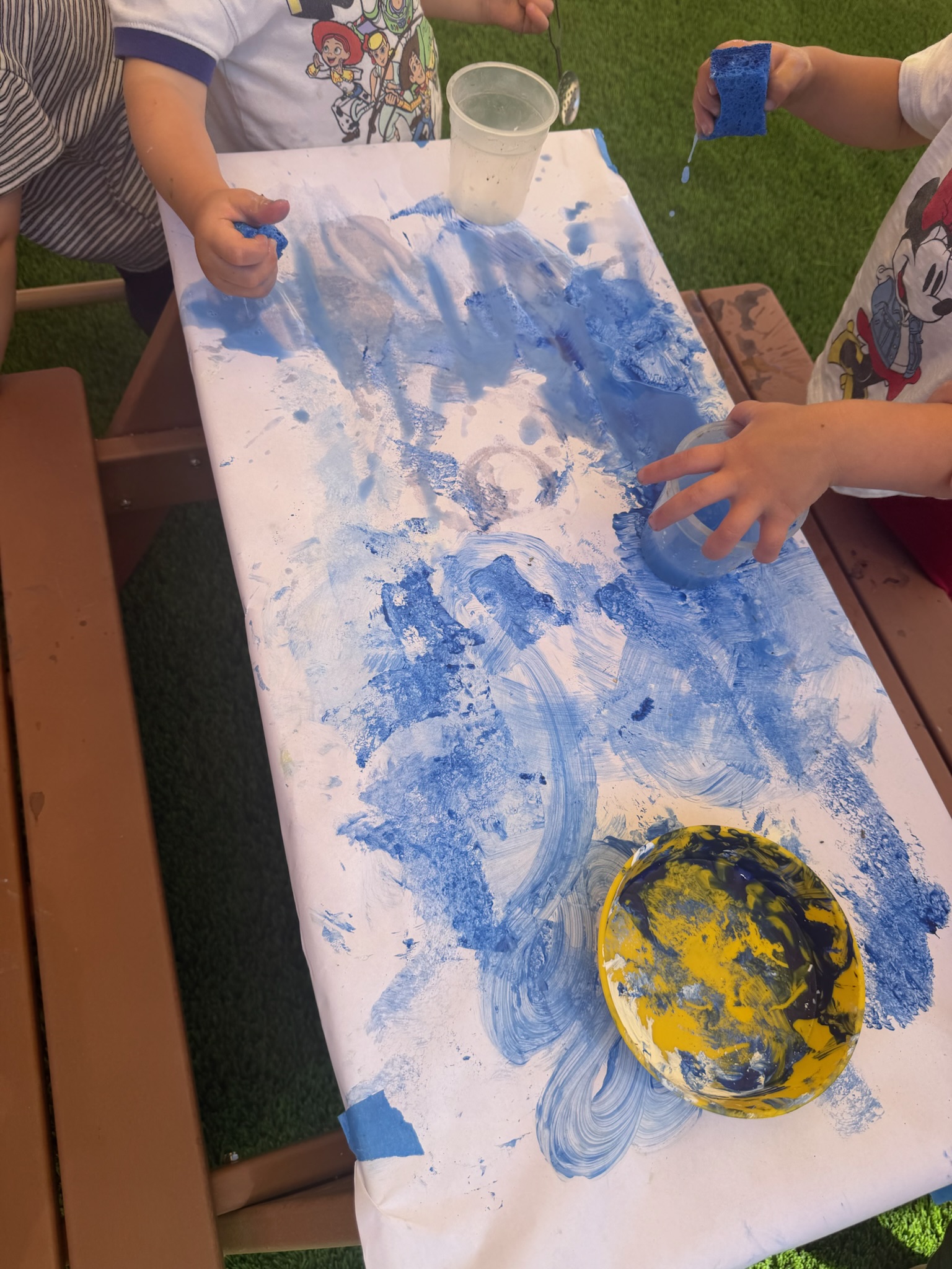 Toddlers doing sponge painting on paper at the outdoor table at Happy Nook